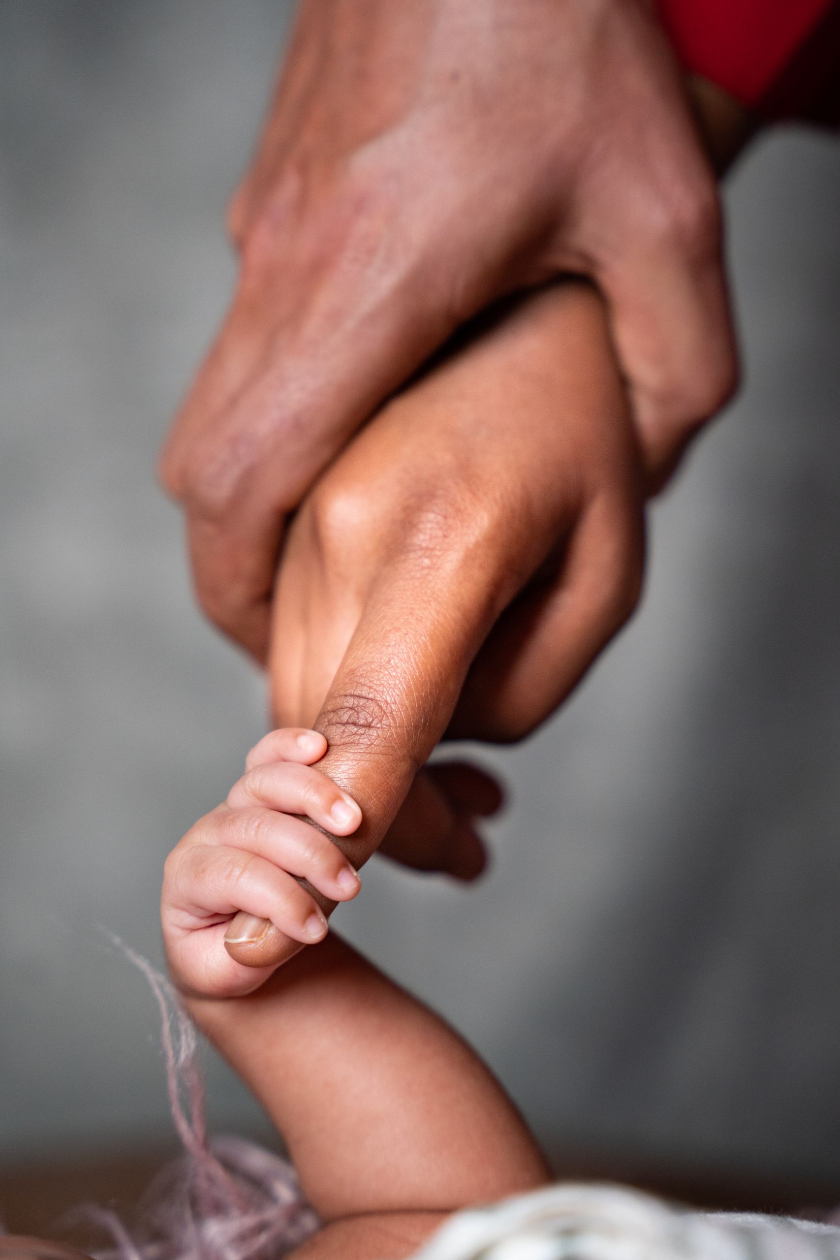 A close-up of an adult and baby holding hands, symbolizing connection and care.